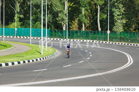 Female sportsman cyclist riding racing bicycle. Woman cycling on countryside summer road or highway. Training for triathlon or cycling competition. Wide angle. Female sportsman cyclist riding racing bicycle. Woman cycling on countryside summer road or highway. Training for triathlon or cycling competition. Wide angle. 138408610