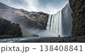 A colossal waterfall thunders down a sheer cliff face, creating mist and spray, with a person standing at the base enjoying the natural beauty A colossal waterfall thunders down a sheer cliff face, creating mist and spray, with a person standing at the base enjoying the natural beauty 138408841