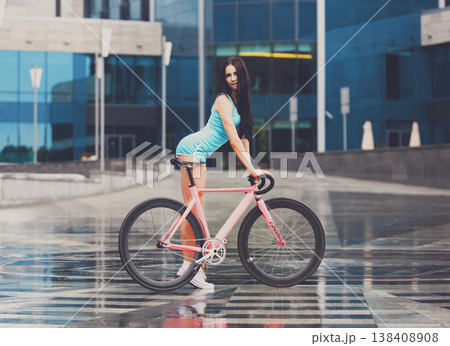 Sexy girl with bicycle. Young slim sexy sportive woman in blue shorts and white snickers long-haired, sensual posing with pink fix bicycle in urban city enviroment. Soft toned. Sexy girl with bicycle. Young slim sexy sportive woman in blue shorts and white snickers long-haired, sensual posing with pink fix bicycle in urban city enviroment. Soft toned. 138408908
