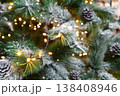 Christmas tree holiday background. Xmas magic and beauty. Fluffy pine tree branches with pinecones, sprinkled with snow and decorated with shiny garland, closeup 138408946