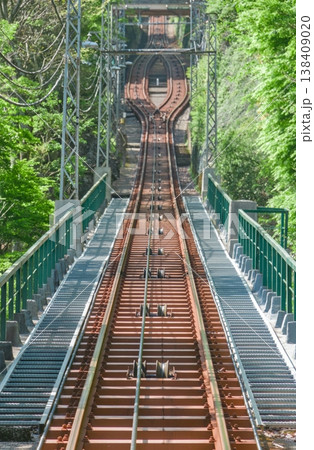 新緑の山を登るケーブルカーの線路、急勾配とすれ違い地点、縦位置 138409020