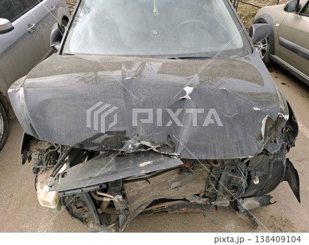 A black car is damaged from a collision. The hood is crumpled, the radiator is smashed, and engine parts are exposed. This is seen at a roadside with other vehicles nearby. A black car is damaged from a collision. The hood is crumpled, the radiator is smashed, and engine parts are exposed. This is seen at a roadside with other vehicles nearby. 138409104