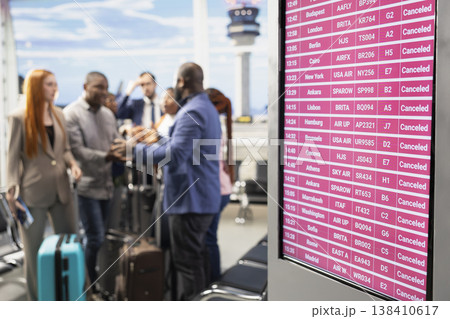 Stranded people reacting to bad news of cancelled flights and suspended departures, chaotic airport scene. Diverse crowd looking at the schedule board in disbelief, ruined travel plans. 138410617