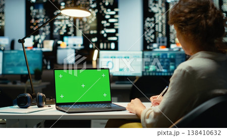 Female analyst uses green screen on laptop and planning new tasks, business administration specialist works at her desk for activity management after hours. Woman alone in the office. Camera B. Female analyst uses green screen on laptop and planning new tasks, business administration specialist works at her desk for activity management after hours. Woman alone in the office. Camera B. 138410632