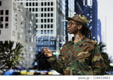 Army soldier patrolling on city street sidewalk, tasked with town security. African american female military officer in camouflage uniform strolling on metropolitan area boulevard, defense concept Army soldier patrolling on city street sidewalk, tasked with town security. African american female military officer in camouflage uniform strolling on metropolitan area boulevard, defense concept 138410663