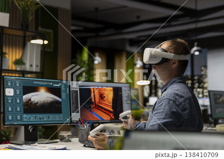 Male game developer using VR glasses and AI tech to design a spaceship for a video game, moving assets in 3D software for the spatial environment. Virtual development for the internet. Male game developer using VR glasses and AI tech to design a spaceship for a video game, moving assets in 3D software for the spatial environment. Virtual development for the internet. 138410709