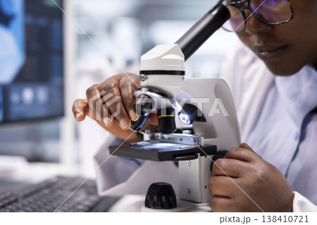 Close up of black expert analyzing samples in chemistry lab with microscope and observation tools. Scientist advancing genetics research, combining pathology analysis with biochemistry studies. 138410721