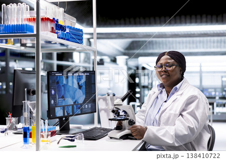 Scientist analyzing samples in laboratory setting with microscope and chemicals. Female expert advancing genetics research, combining laboratory analysis with biochemistry studies. Scientist analyzing samples in laboratory setting with microscope and chemicals. Female expert advancing genetics research, combining laboratory analysis with biochemistry studies. 138410722