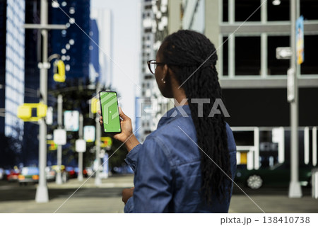 Green screen smartphone navigation app used by woman to orientate around urban landscape. African american girl using digital map application on mockup mobile phone while walking on city streets Green screen smartphone navigation app used by woman to orientate around urban landscape. African american girl using digital map application on mockup mobile phone while walking on city streets 138410738