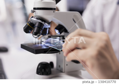 Close up of man researcher investigates tray samples under optical microscope. Observation tool with magnifying glass highlight biochemistry and medical research, bioengineering. 138410770