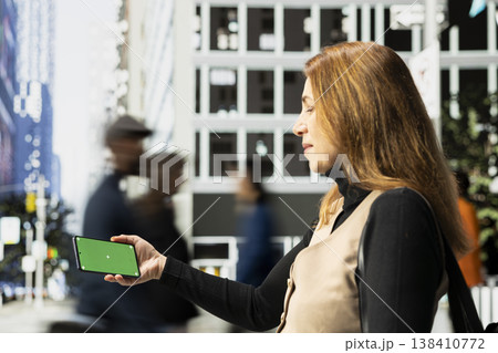 Horizontal green screen on phone held by businesswoman near urban motion of diverse pedestrians crowd on downtown street captures city life, diversity and the daily realistic routine. 138410772