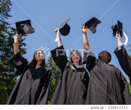 Young women of different nationalities pull graduation caps up. Young women of different nationalities pull graduation caps up. 138411311