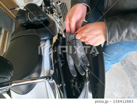 A young man puts on motorcycle gloves as part of his riding gear with a motorcycle standing nearby. Personal safety and protection measures on the road. High quality photo A young man puts on motorcycle gloves as part of his riding gear with a motorcycle standing nearby. Personal safety and protection measures on the road. High quality photo 138412665