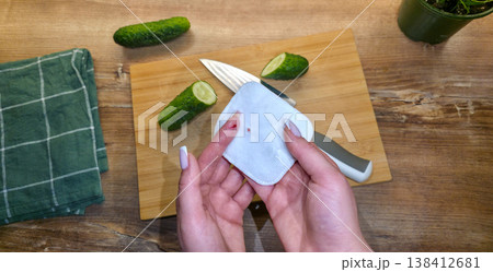 A woman is treating a knife cut on her finger in close-up against the background of a cutting board, cucumbers, and a knife in the kitchen. High quality photo A woman is treating a knife cut on her finger in close-up against the background of a cutting board, cucumbers, and a knife in the kitchen. High quality photo 138412681
