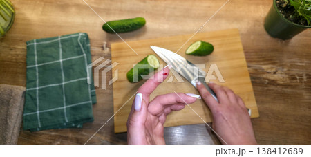 A close-up of a finger cut on the hand with a knife against the background of a cutting board, cucumbers, and a knife in the kitchen. High quality photo 138412689