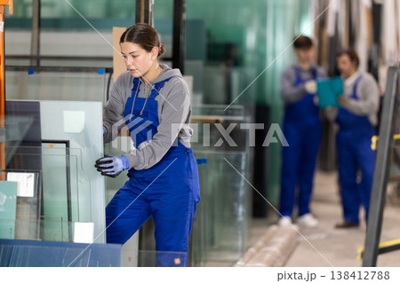 Girl glazer employee in blue overall works in glass processing shop Girl glazer employee in blue overall works in glass processing shop 138412788