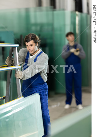 Man glazer employee in blue overall works in glass processing shop Man glazer employee in blue overall works in glass processing shop 138412804