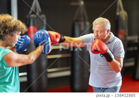 Older amateur boxer working pads with partner 138412805