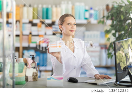 Female pharmacist working at computer offering pills Female pharmacist working at computer offering pills 138412883