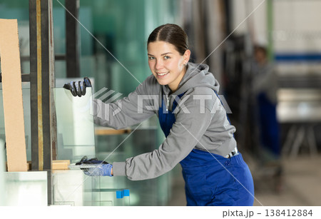 Girl glazer employee in blue overall works in glass processing shop 138412884
