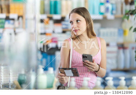 Girl in summer clothes scans code on cosmetics to check expiration date 138412890