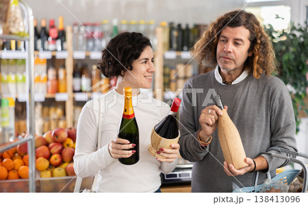 Husband and wife shopping together at supermarket - choosing bottles of wine Husband and wife shopping together at supermarket - choosing bottles of wine 138413096