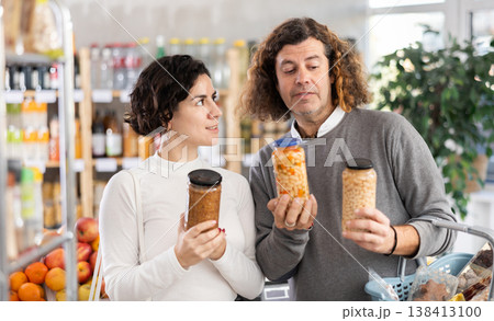 In store, couple near counter are looking at canned beans and lentils 138413100