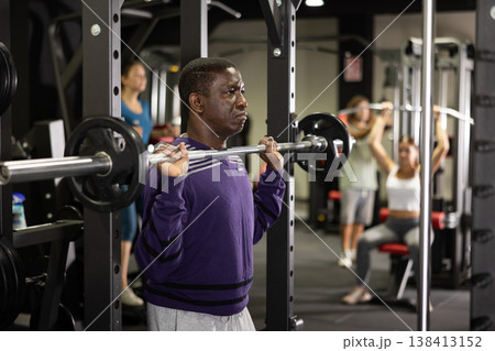 African man doing squats with weight using half rack in gym 138413152