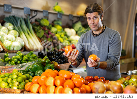 Adult man buyer chooses tangerines in shop Adult man buyer chooses tangerines in shop 138413162