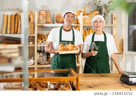 European man and senior woman sellers stands in trading hall of bakery European man and senior woman sellers stands in trading hall of bakery 138413232