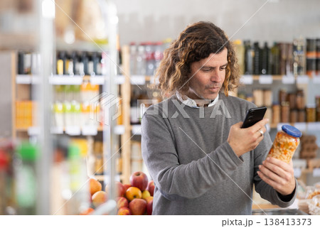 Checking expiration date of beans - male shopper scans QR code on label of jar canned beans using smartphone Checking expiration date of beans - male shopper scans QR code on label of jar canned beans using smartphone 138413373