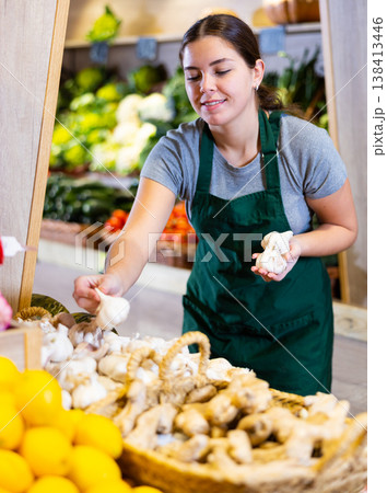 Female seller holding garlic standing in fruit and vegetable section of supermarket Female seller holding garlic standing in fruit and vegetable section of supermarket 138413446