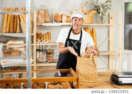 Male baker hands paper bag with fresh baked goods to customer 138413451