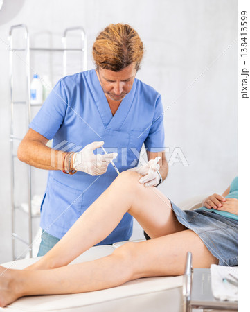 Male doctor making injection in leg of woman patient 138413599