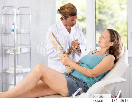 Male beautician giving consultation to woman patient with mirror in aesthetic clinic Male beautician giving consultation to woman patient with mirror in aesthetic clinic 138413618