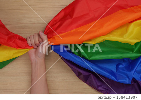 Hand holding LGBTQ pride flag on wooden surface 138413907
