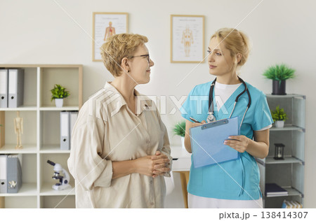 Nurse and female elderly patient standing together during consultation in clinic. 138414307