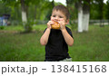 Three year old boy eats cheeseburger outdoors and looks at camera portrait 4k 138415168