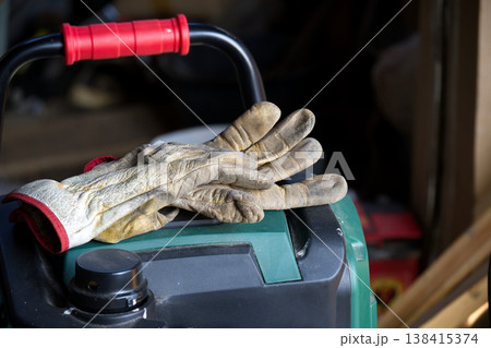 Pair of worn leather work gloves resting on a green and black machine 138415374