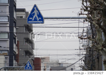 日本の都市景観。電線が張り巡らされた空と重なり合う横断歩道の交通標識 日本の都市景観。電線が張り巡らされた空と重なり合う横断歩道の交通標識 138415427