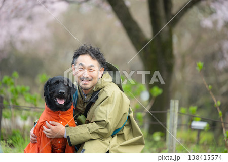 レインコートを着る犬と飼い主　雨の中で犬と散歩する男性の癒しと自然を感じる春の散歩シーンカメラ目線 138415574