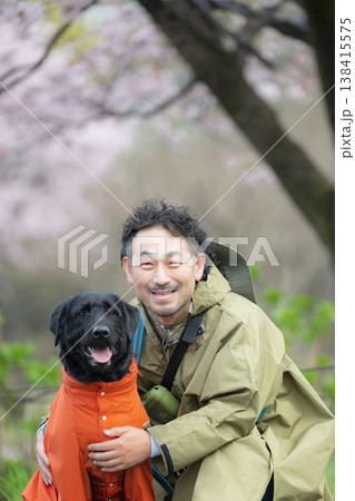 レインコートを着る犬と飼い主　雨の中で犬と散歩する男性の癒しと自然を感じる春の散歩シーンカメラ目線 138415575
