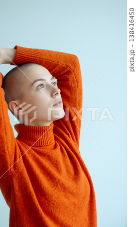 Young bald woman in orange turtleneck sweater looking up with hope - Pastel blue background 138416450