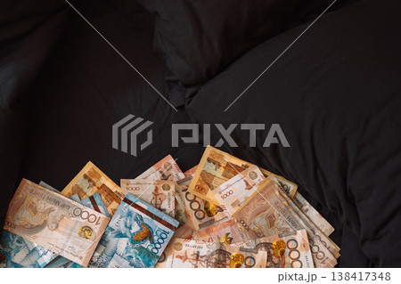 Close up pile of Kazakhstani tenge banknotes on dark couch, money stash concept Close up pile of Kazakhstani tenge banknotes on dark couch, money stash concept 138417348