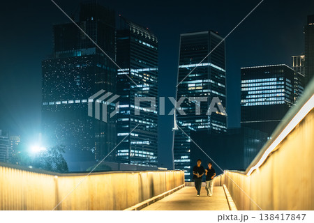 People walking on illuminated park walkway with Bangkok skyline at night, Urban scene with pedestrians strolling along lit path in Benchakitti, Thailand People walking on illuminated park walkway with Bangkok skyline at night, Urban scene with pedestrians strolling along lit path in Benchakitti, Thailand 138417847