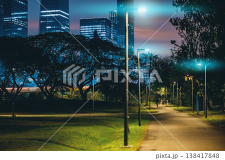 Night park alley with lights and skyline in Benchakitti Bangkok park with people walking, Benjakitti walkway with illumination and modern city skyscrapers buildings at dusk Night park alley with lights and skyline in Benchakitti Bangkok park with people walking, Benjakitti walkway with illumination and modern city skyscrapers buildings at dusk 138417848