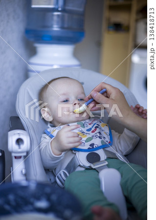 Baby Feeding Moment. Tender Scene Of Baby Eating With Caregiver Nearby In Cozy Setting. Delightful Image Of Baby Being Fed With Care In Comfortable Kitchen Area verical Baby Feeding Moment. Tender Scene Of Baby Eating With Caregiver Nearby In Cozy Setting. Delightful Image Of Baby Being Fed With Care In Comfortable Kitchen Area verical 138418713