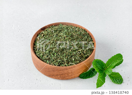 Dried mint leaves in wooden bowl with fresh mint on white background. Dried mint leaves in wooden bowl with fresh mint on white background. 138418740
