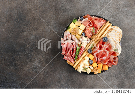 Charcuterie board with assorted cheeses, cured meats, crackers, nuts, berries on dark background. Top view. Copy space. Charcuterie board with assorted cheeses, cured meats, crackers, nuts, berries on dark background. Top view. Copy space. 138418743