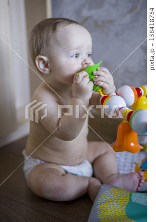 Caucasian Baby Mouthing Green Teether While Seated, Strong Chewing Motion Visible, Bright Home Backdrop, Candid Moment Of Sensory Play And Early Oral Development verical Caucasian Baby Mouthing Green Teether While Seated, Strong Chewing Motion Visible, Bright Home Backdrop, Candid Moment Of Sensory Play And Early Oral Development verical 138418784